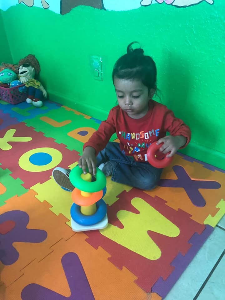 Child playing with a colorful stacking ring toy on a letter mat
