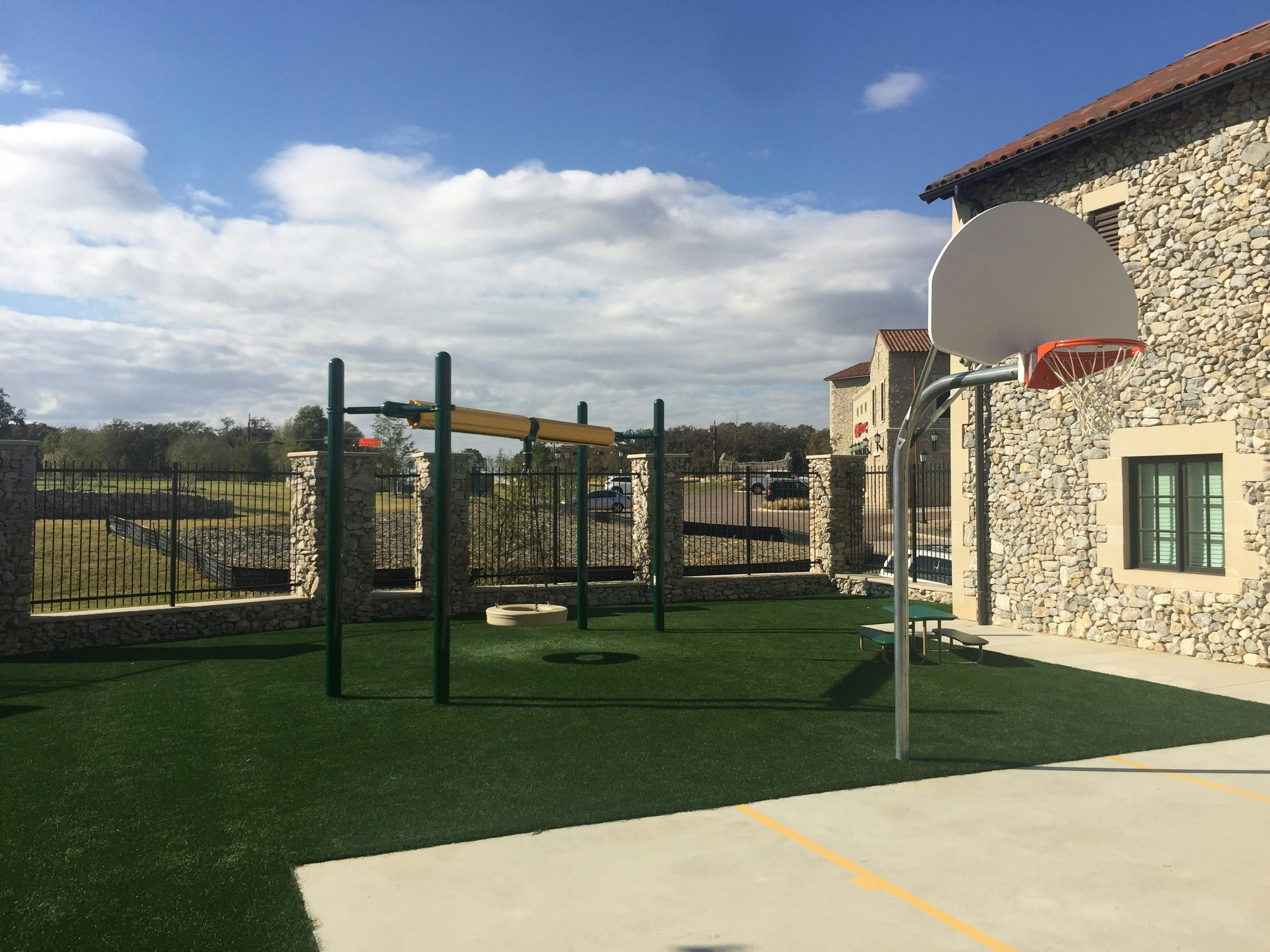 Outdoor playground with monkey bars and a basketball hoop next to a stone building