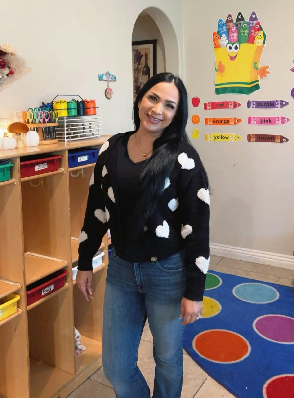 Person in a black sweater with white hearts standing in a classroom