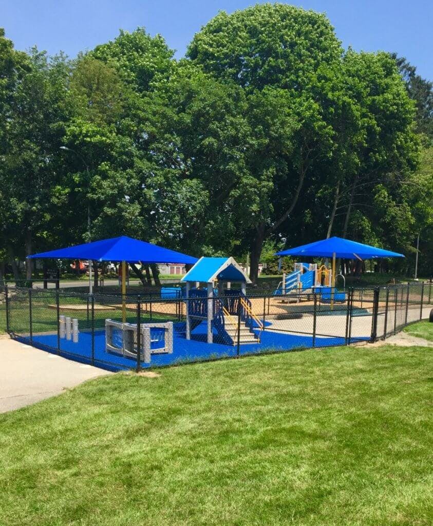 Playground with blue equipment and shade structures, surrounded by a fence