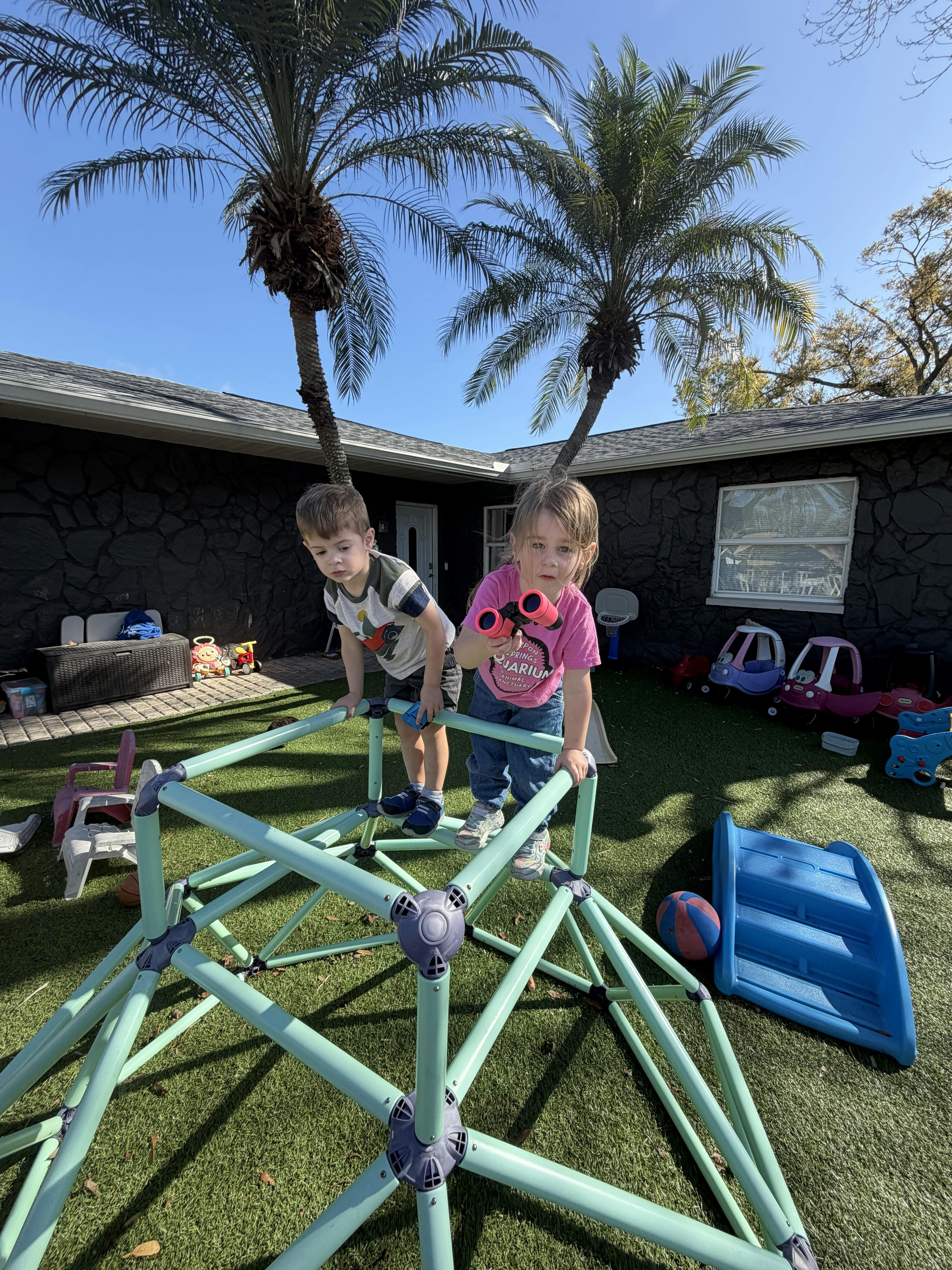 Two children playing on a jungle gym with one holding binoculars