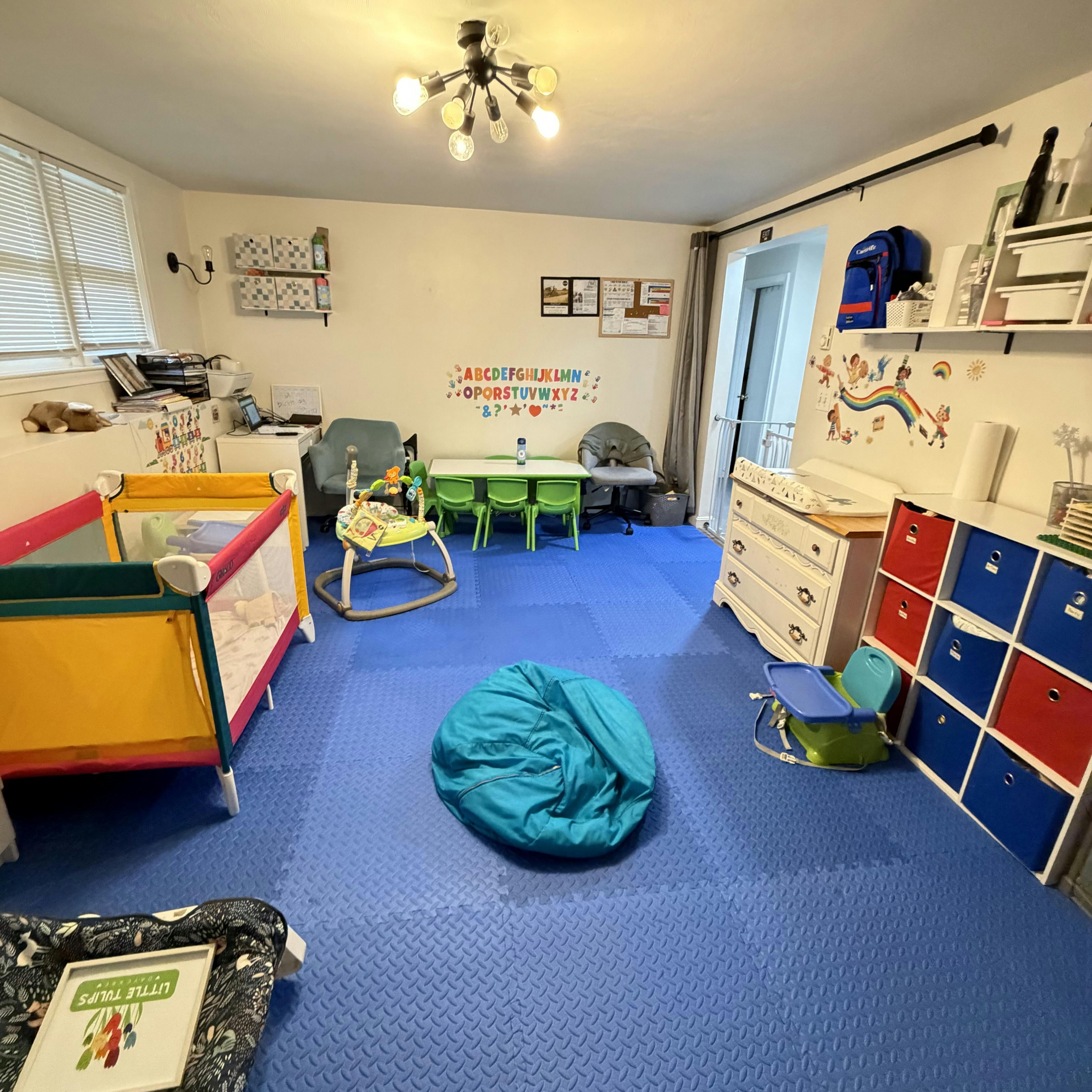 childcare room with playpens, small table and chairs, changing table, and blue floor mats