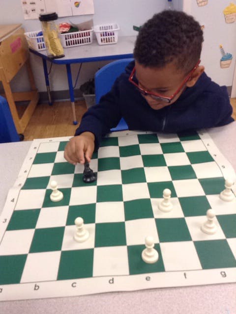 Child in glasses playing chess, moving a black piece