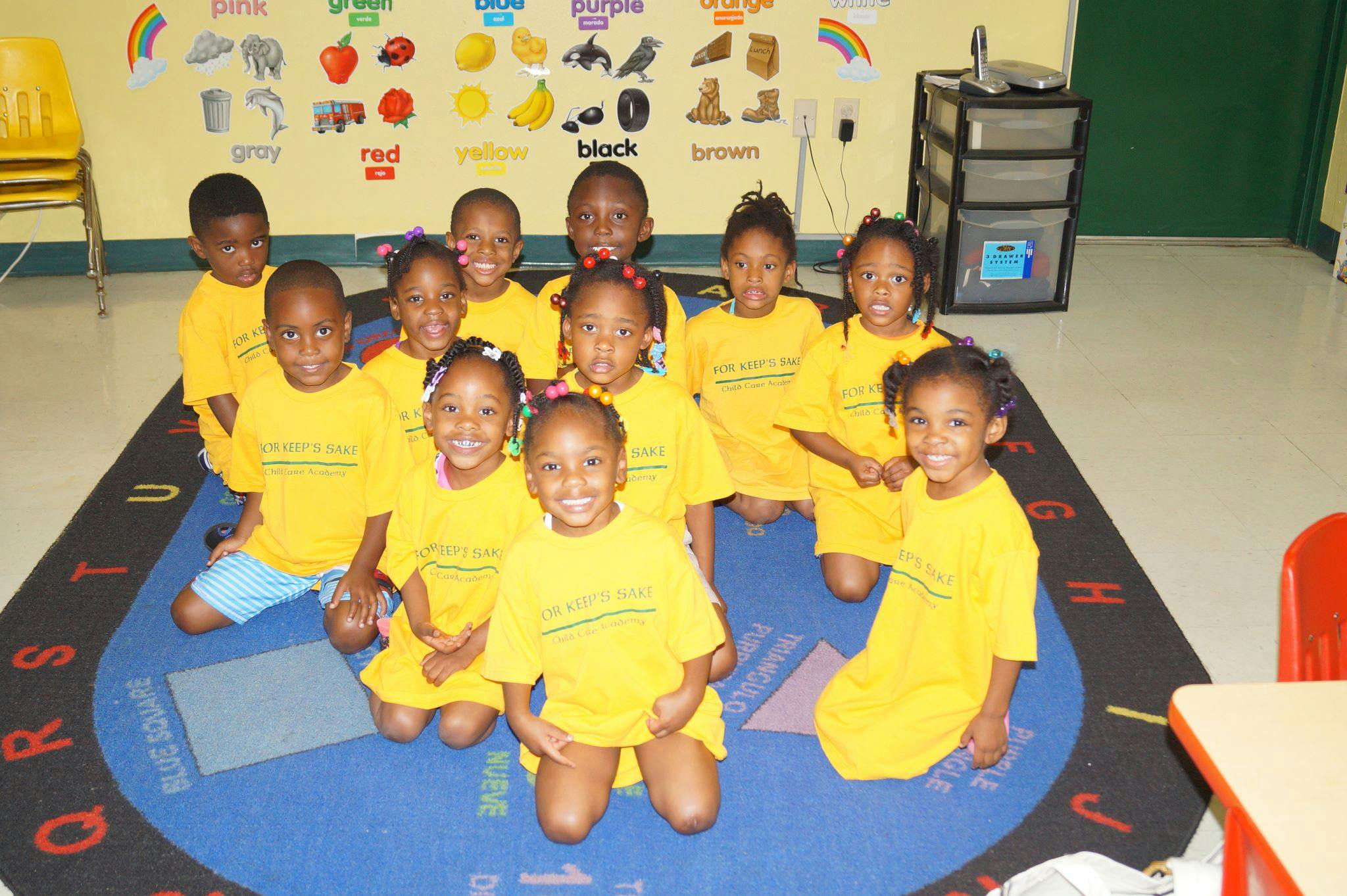 Group of children in yellow shirts sitting on a rug in a classroom