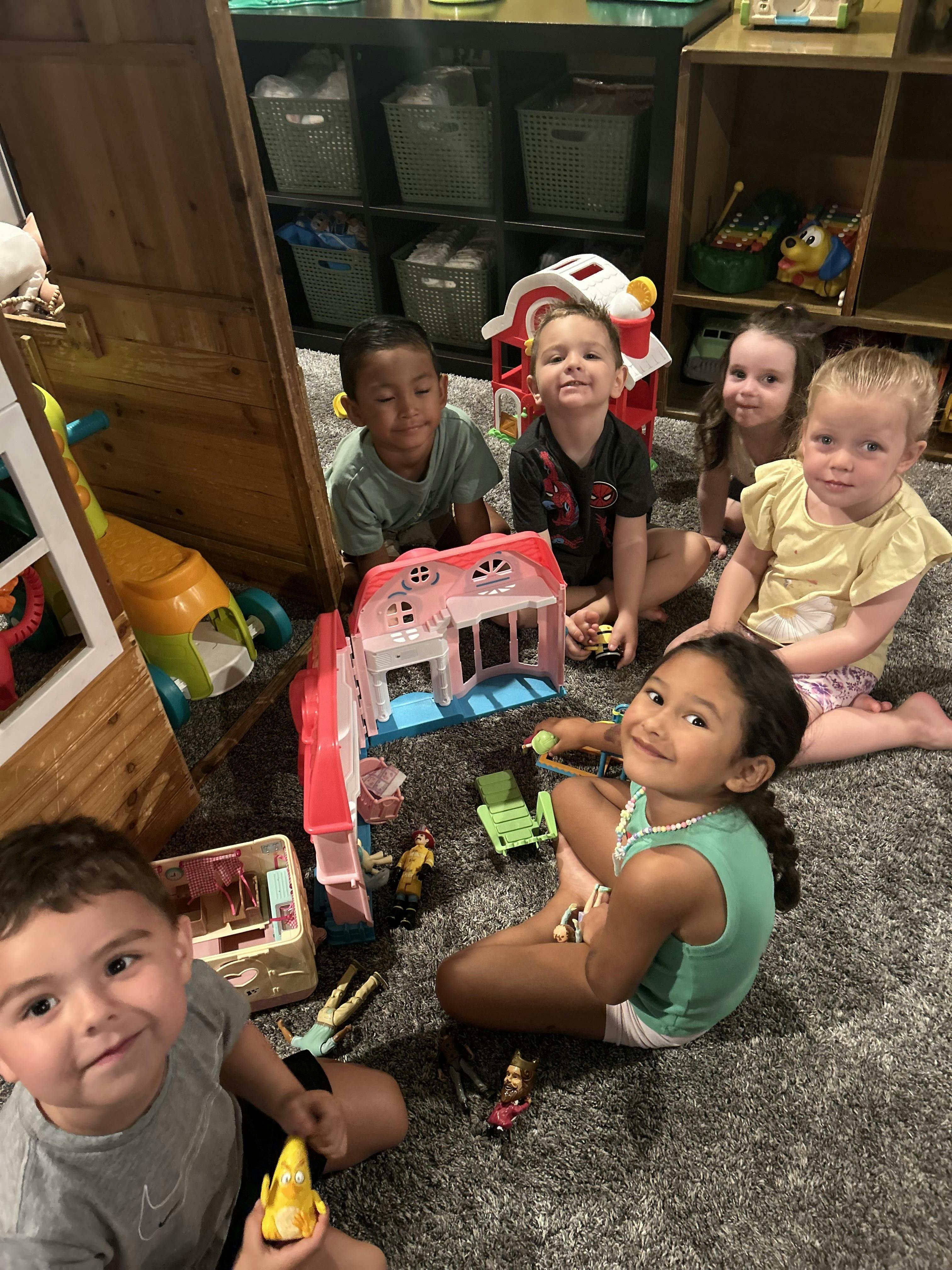 Group of children playing with toy houses and figurines on a carpeted floor