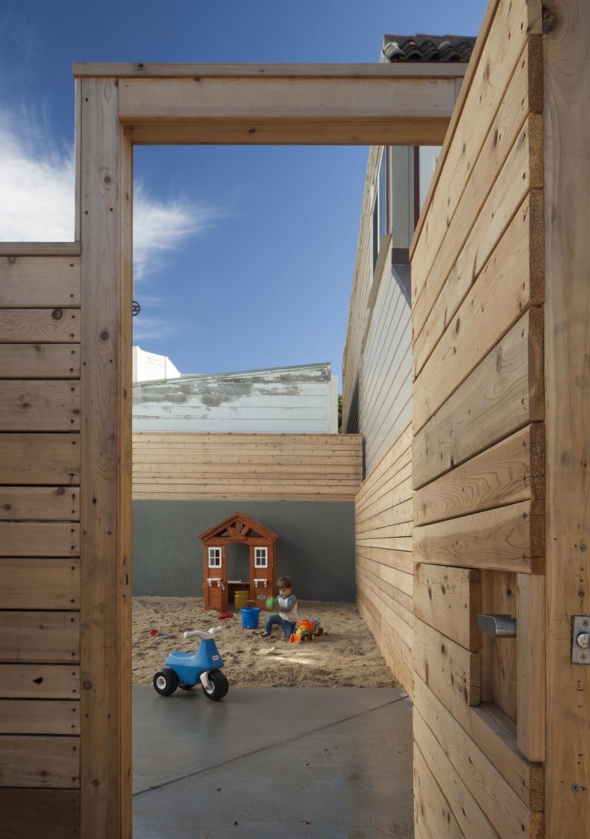 Child playing in a sandbox with a playhouse and tricycle
