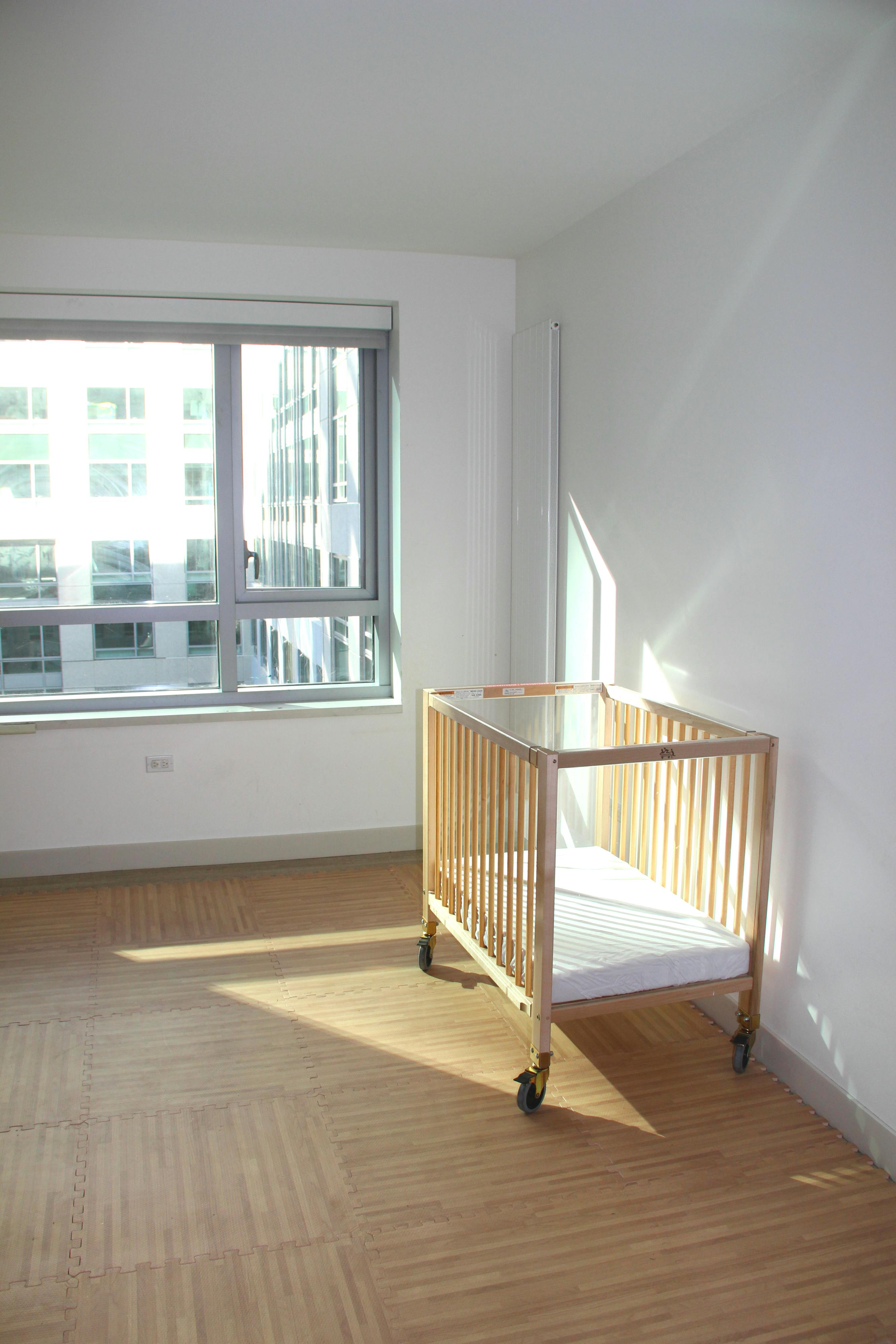 Empty wooden crib with mattress in a room with a large window
