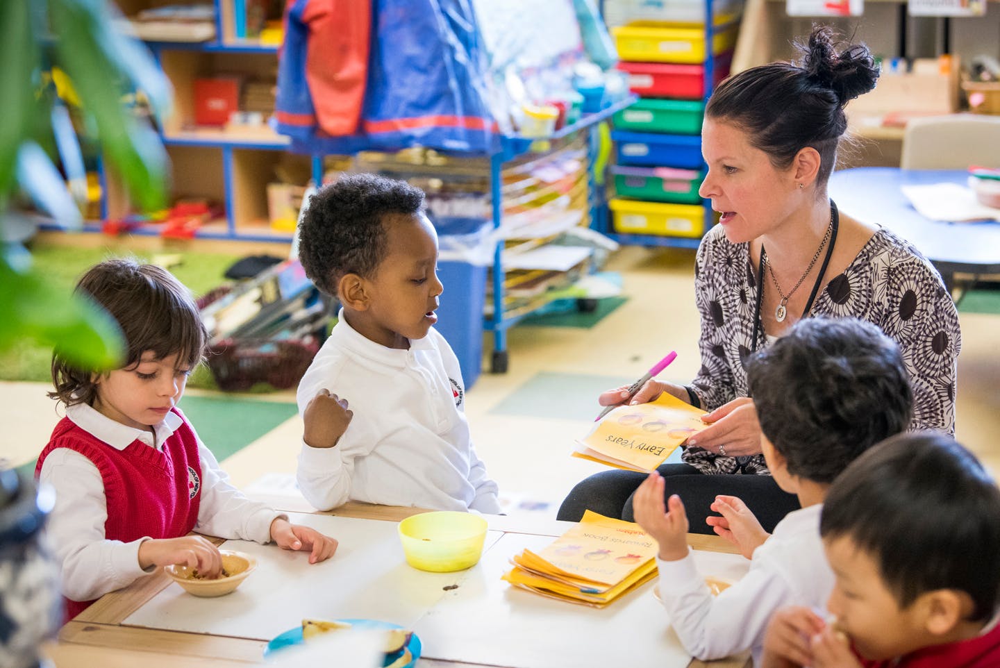 Adult person interacting with multiple children at a table in a classroom