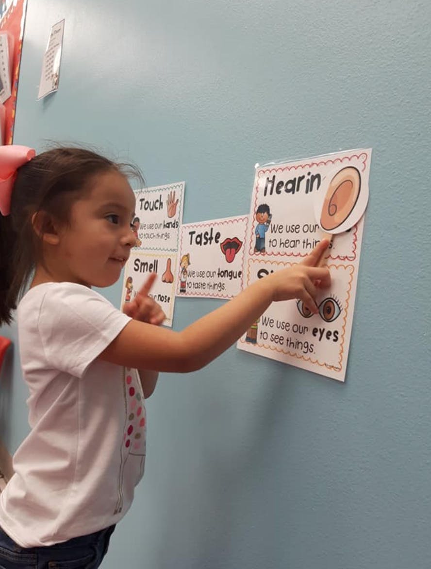 Child pointing at a chart about the five senses in a classroom