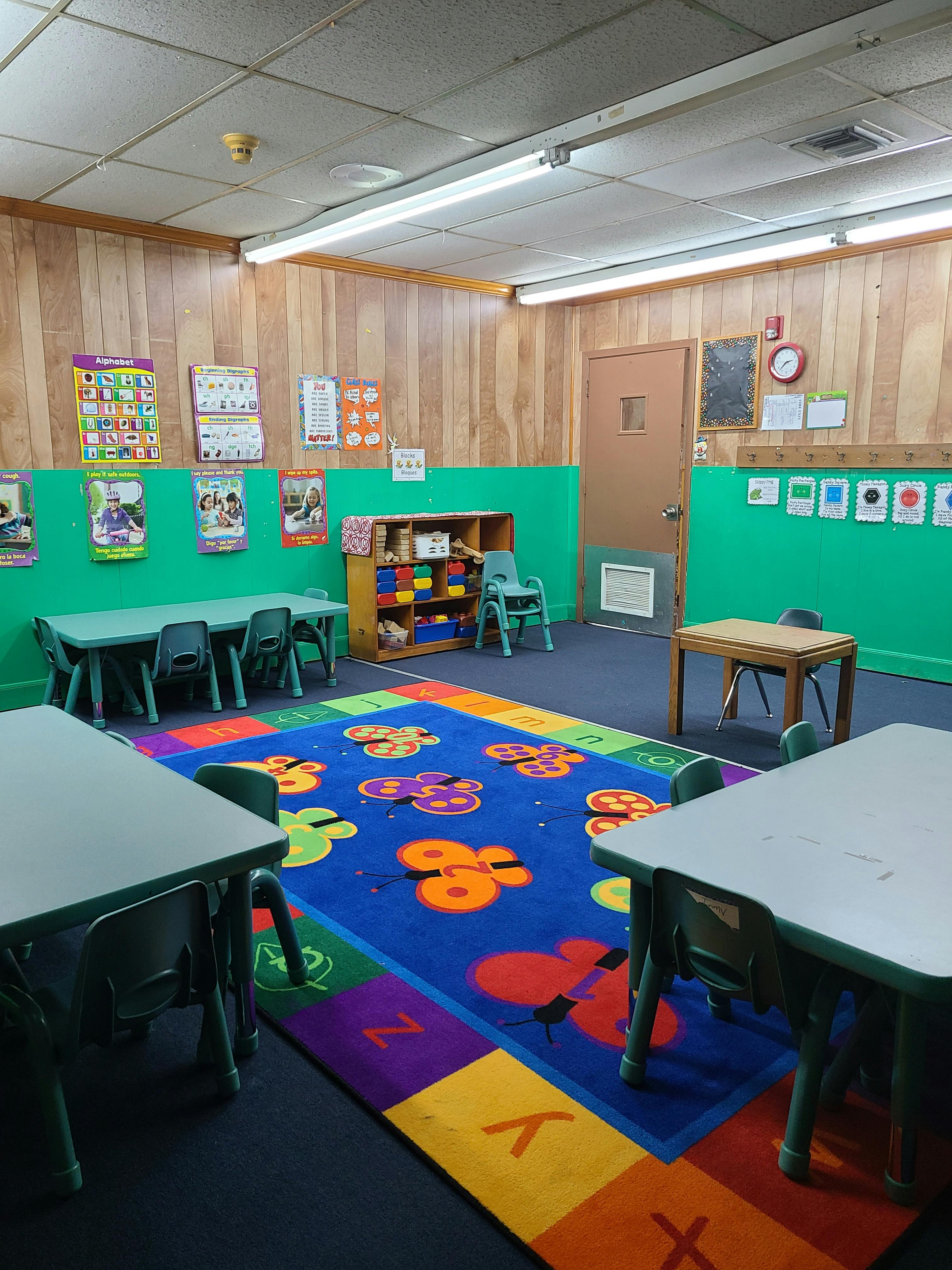 Classroom with small tables and chairs, colorful rug, and posters on walls