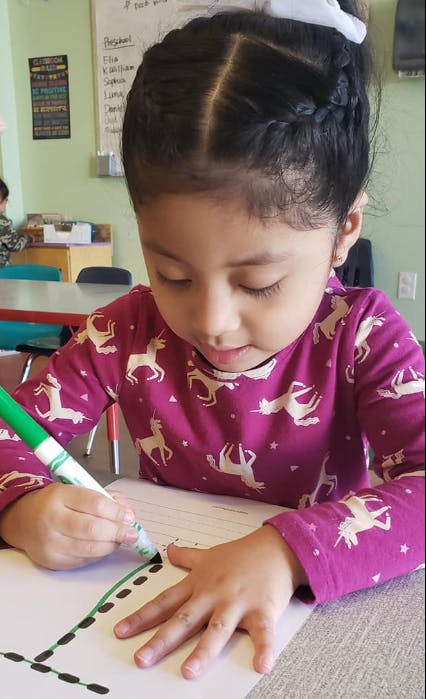 Child drawing on paper with a green marker in a classroom