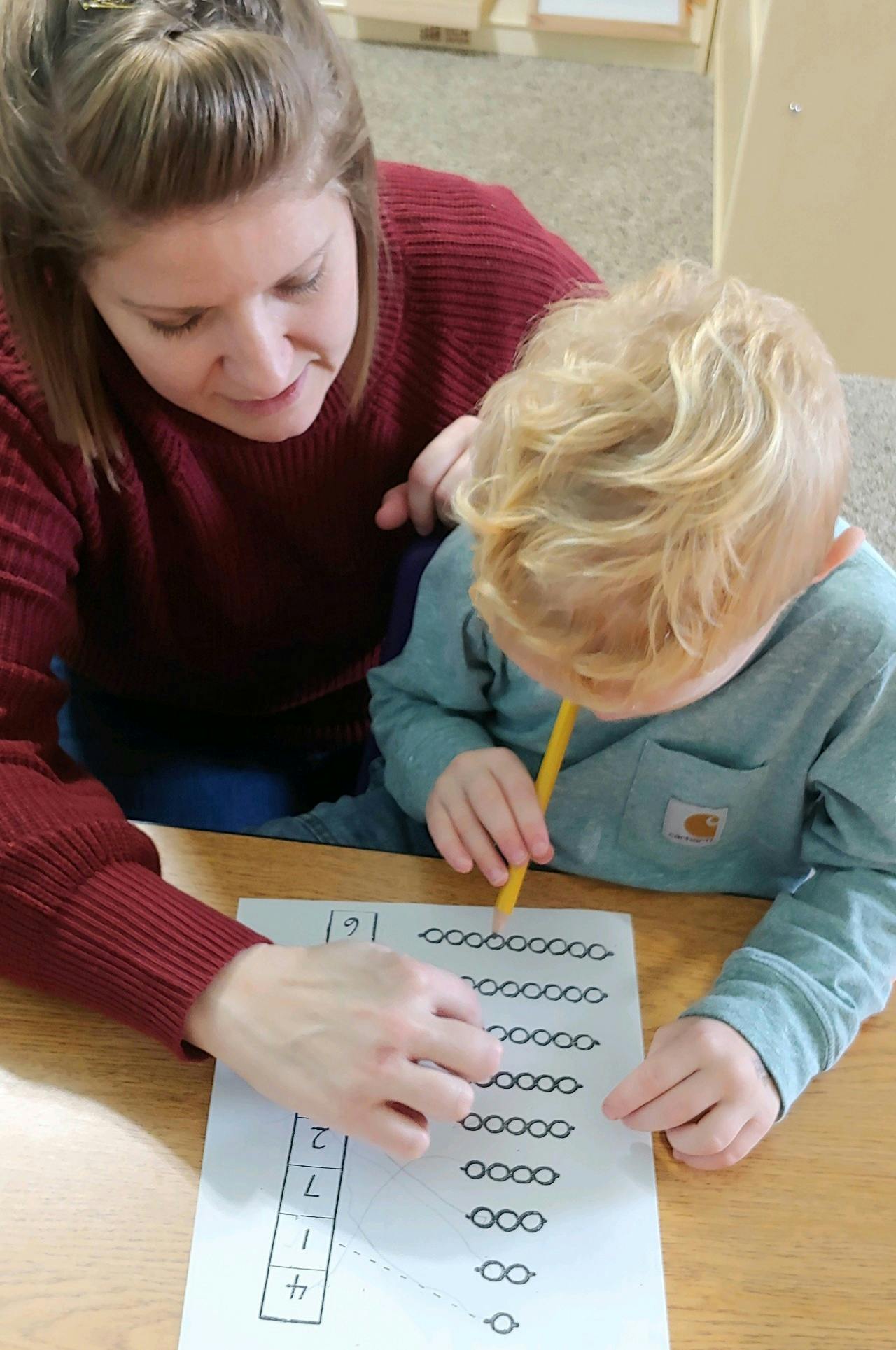 Person helping a child with a pencil trace shapes on a worksheet