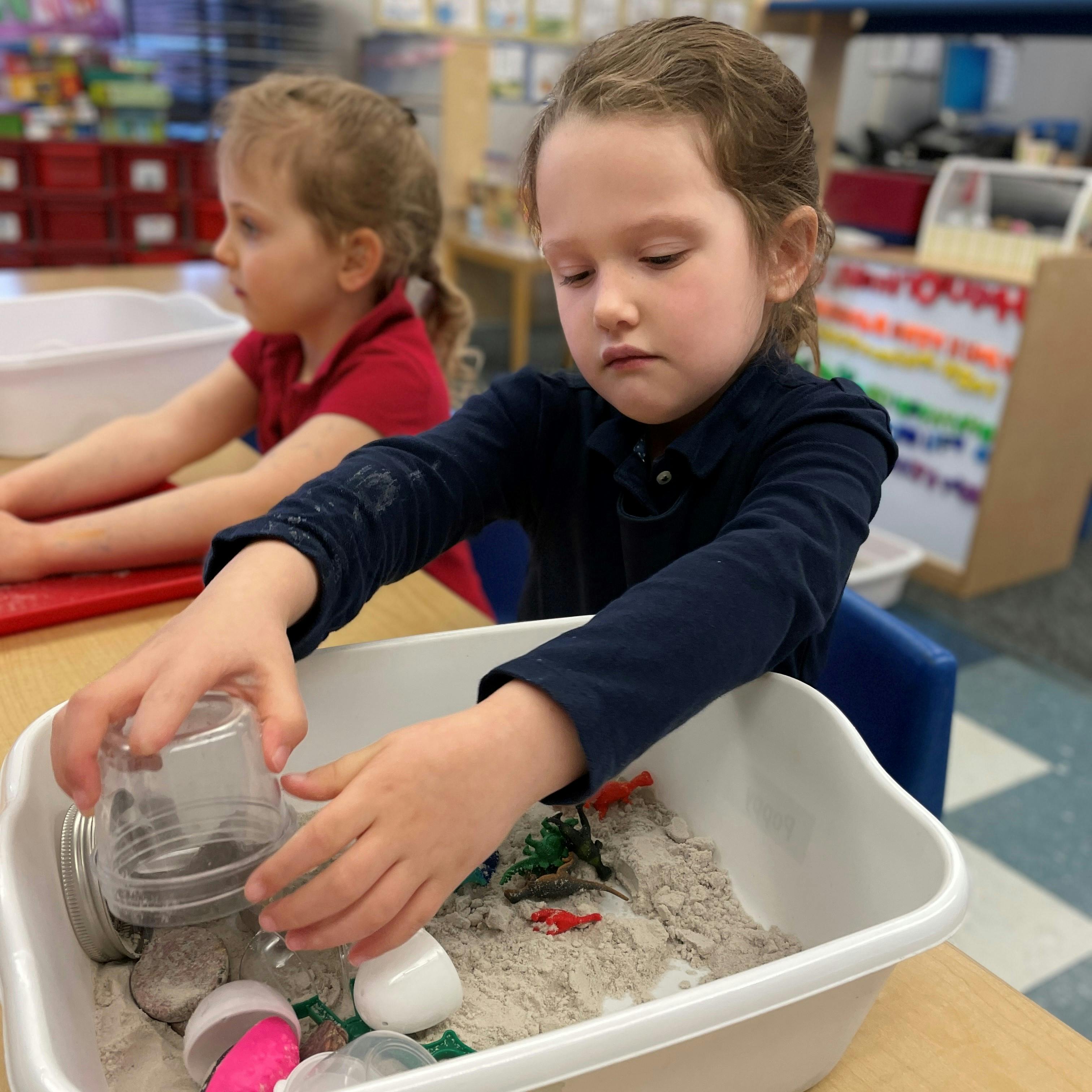 Child playing with sand and small objects in a bin