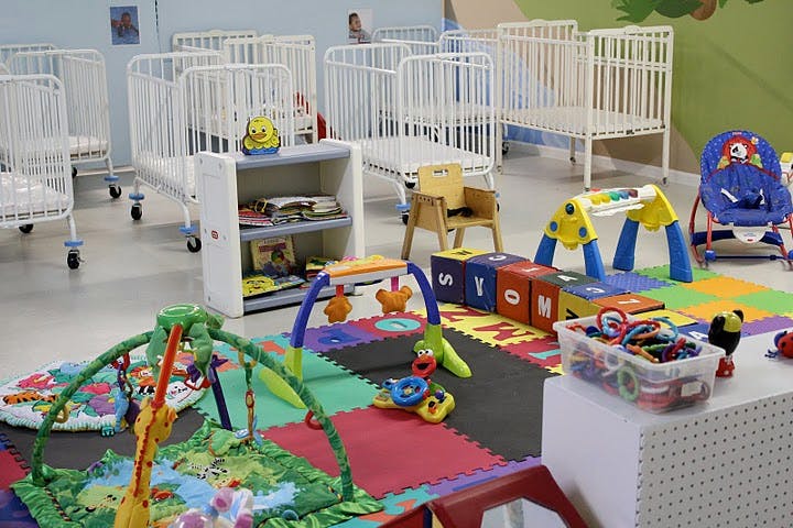 Nursery room with multiple cribs, play mats, and infant toys