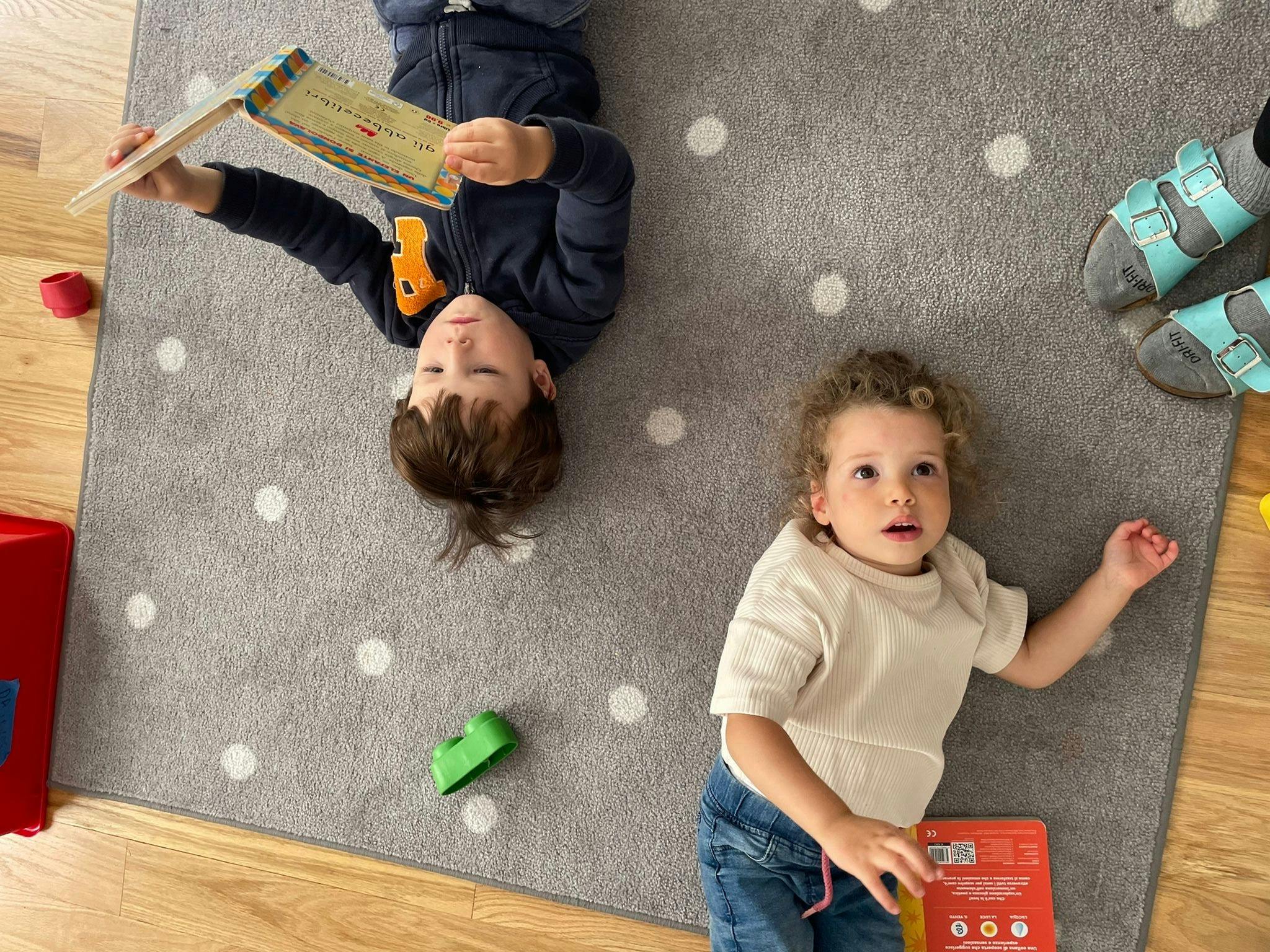 Two children lying on a rug, one reading a book