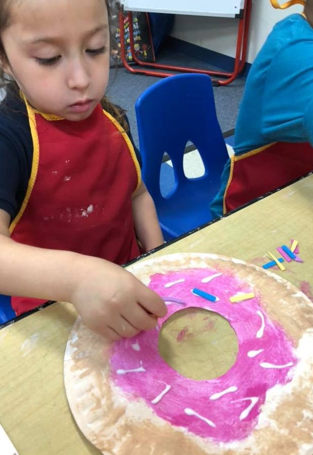 Child in an apron decorating a paper donut with sprinkles