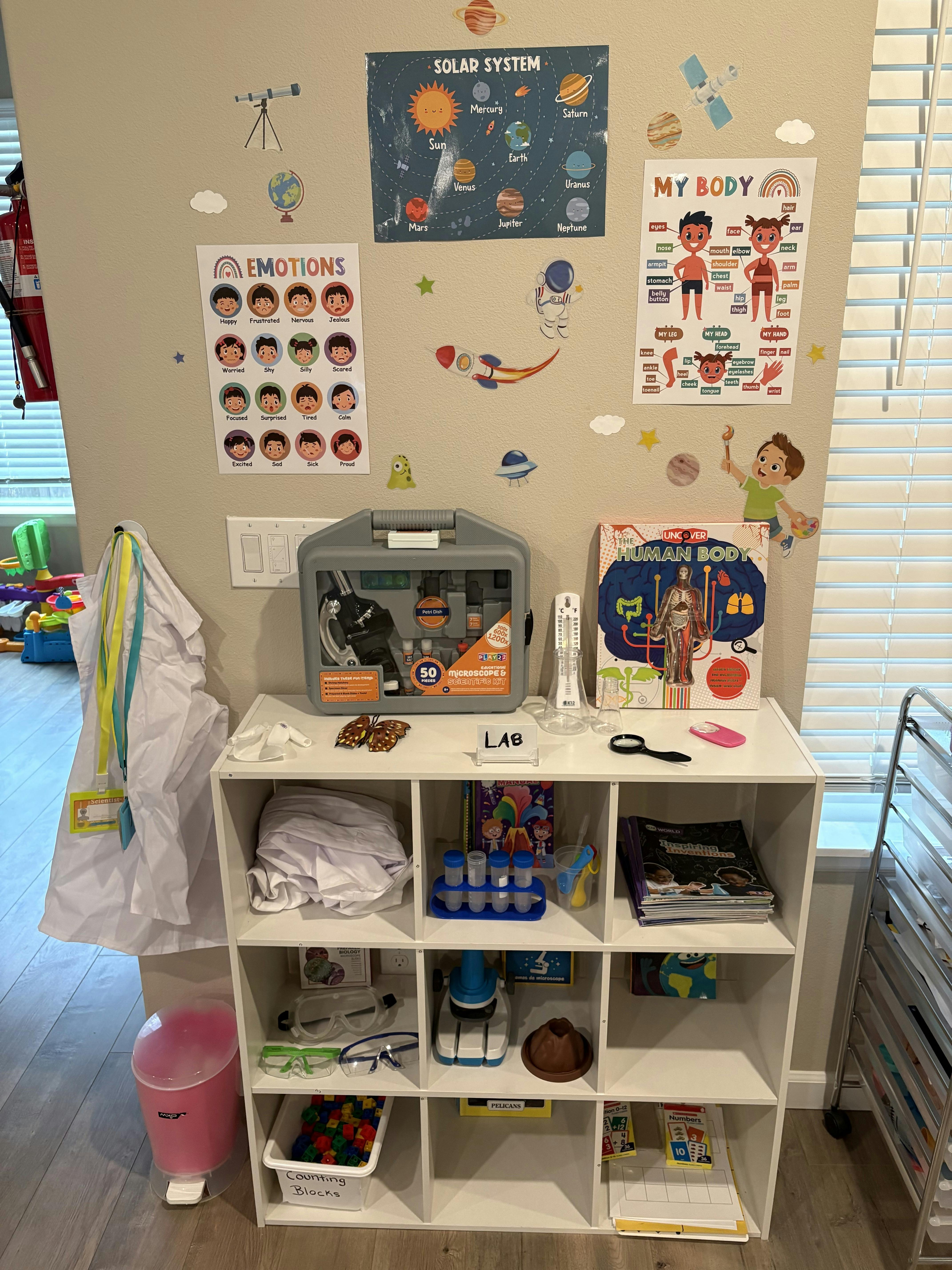 Science-themed learning area with posters, a lab coat, and a storage cube shelf with science kits