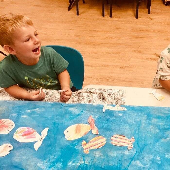 Child playing with paper fish cutouts on a blue surface