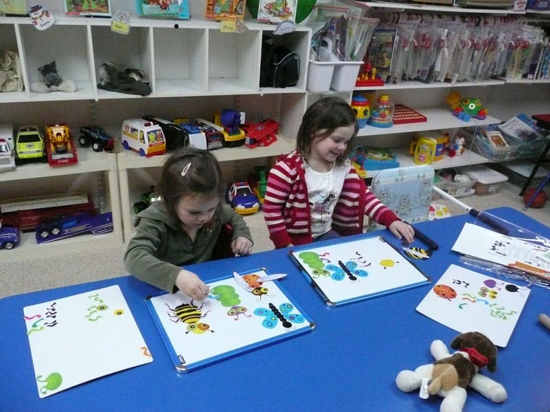 Two children drawing at a blue table in a classroom