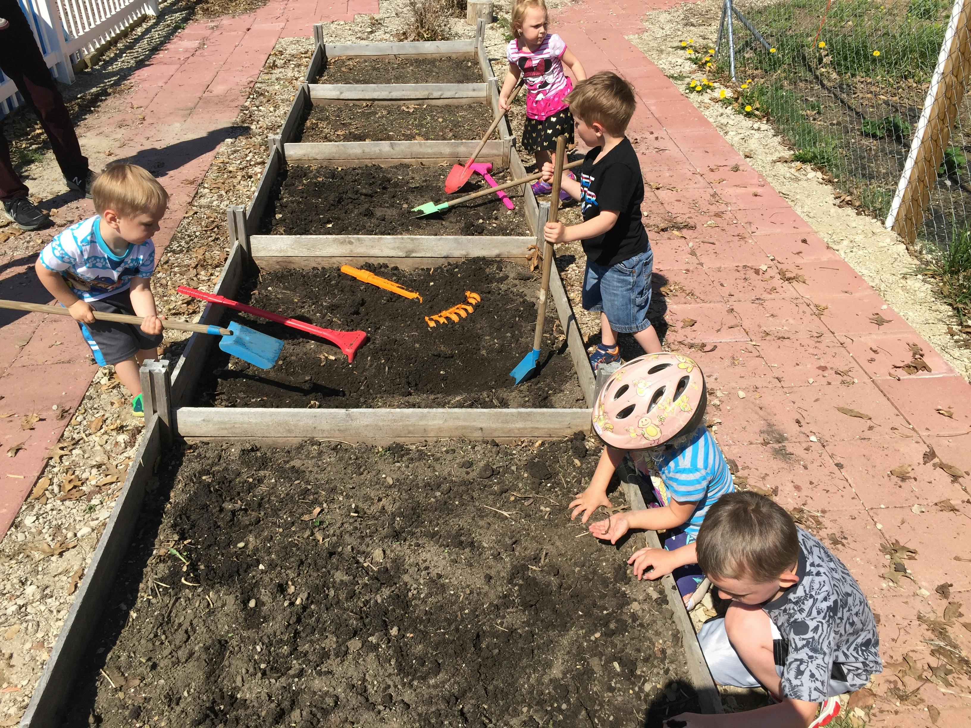 Children playing with gardening tools in raised garden beds