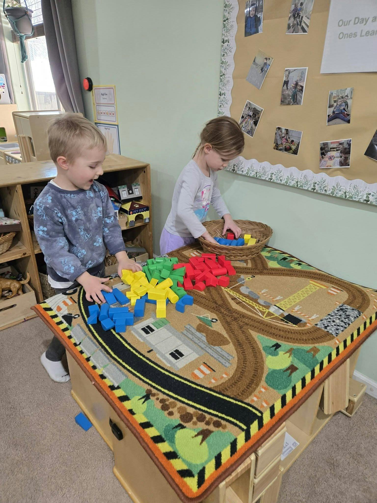 Two children playing with colorful wooden blocks on a rug with roads and buildings