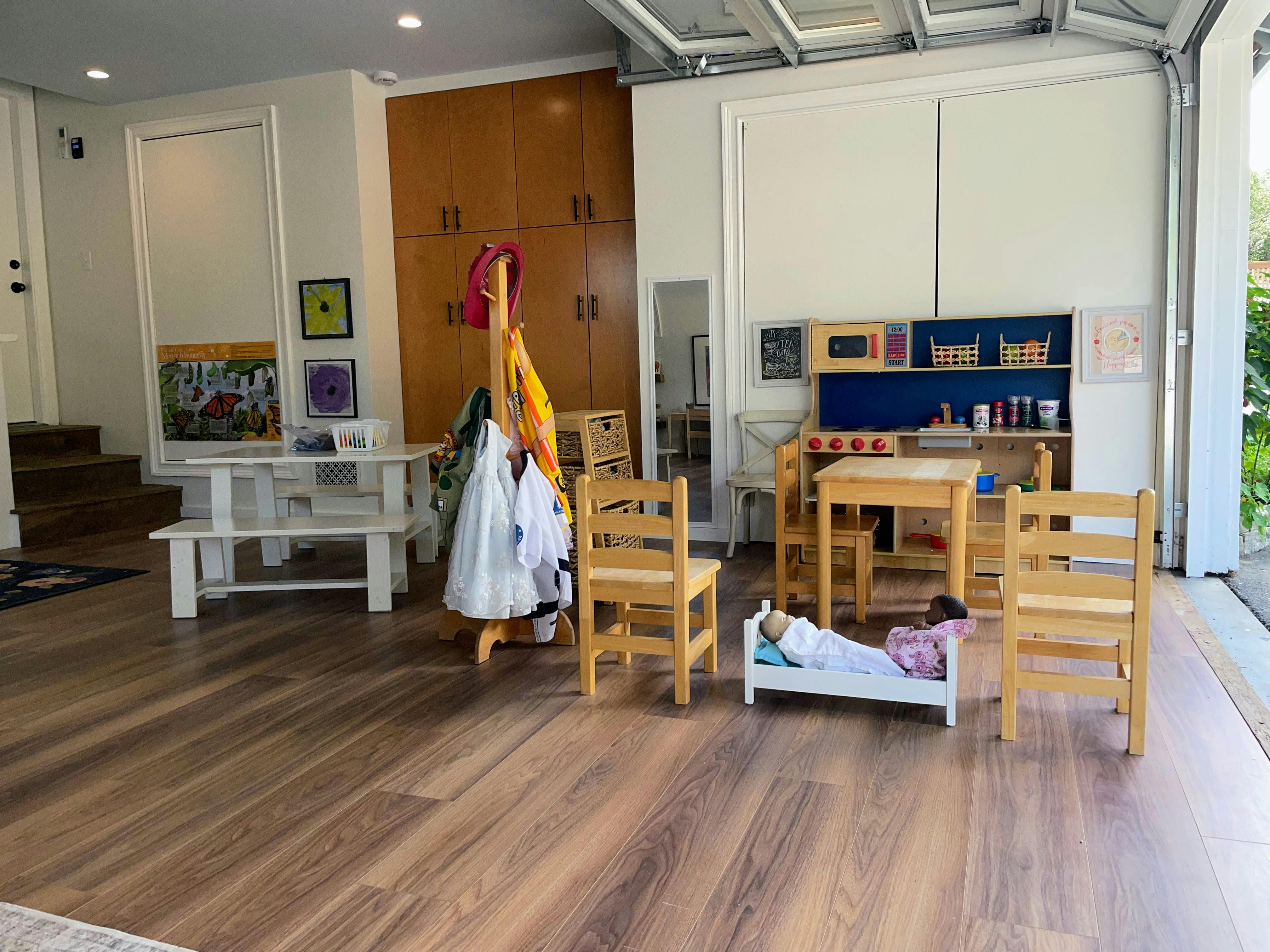 Children's play area with a toy kitchen, doll bed, and wooden table and chairs