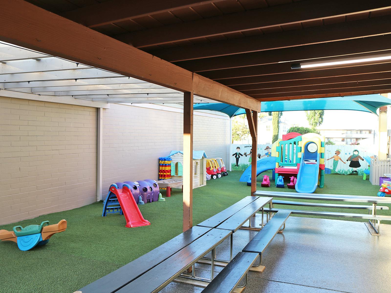 Covered outdoor playground with artificial turf and various colorful play structures