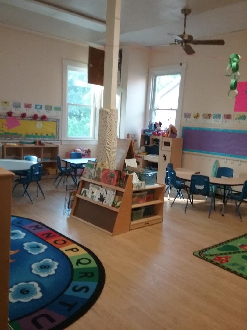 Classroom with small tables and chairs, bookshelves, and alphabet rug