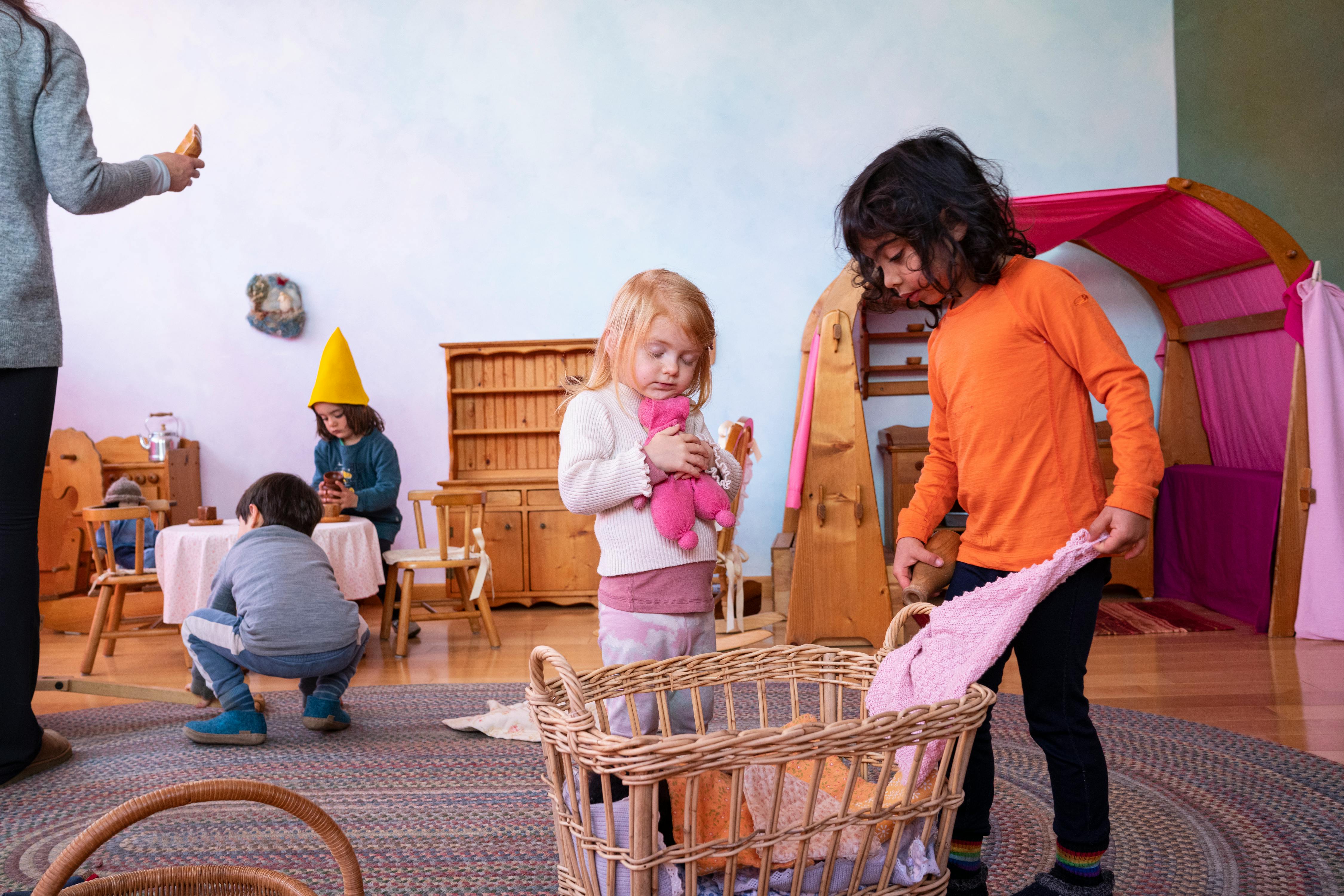 Children playing in a room, one holding a toy, another looking into a basket