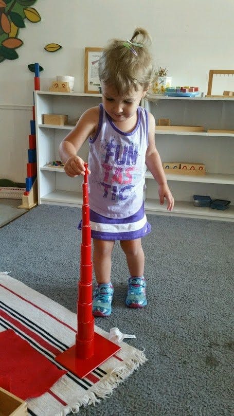 Child playing with a red stacking toy in a classroom