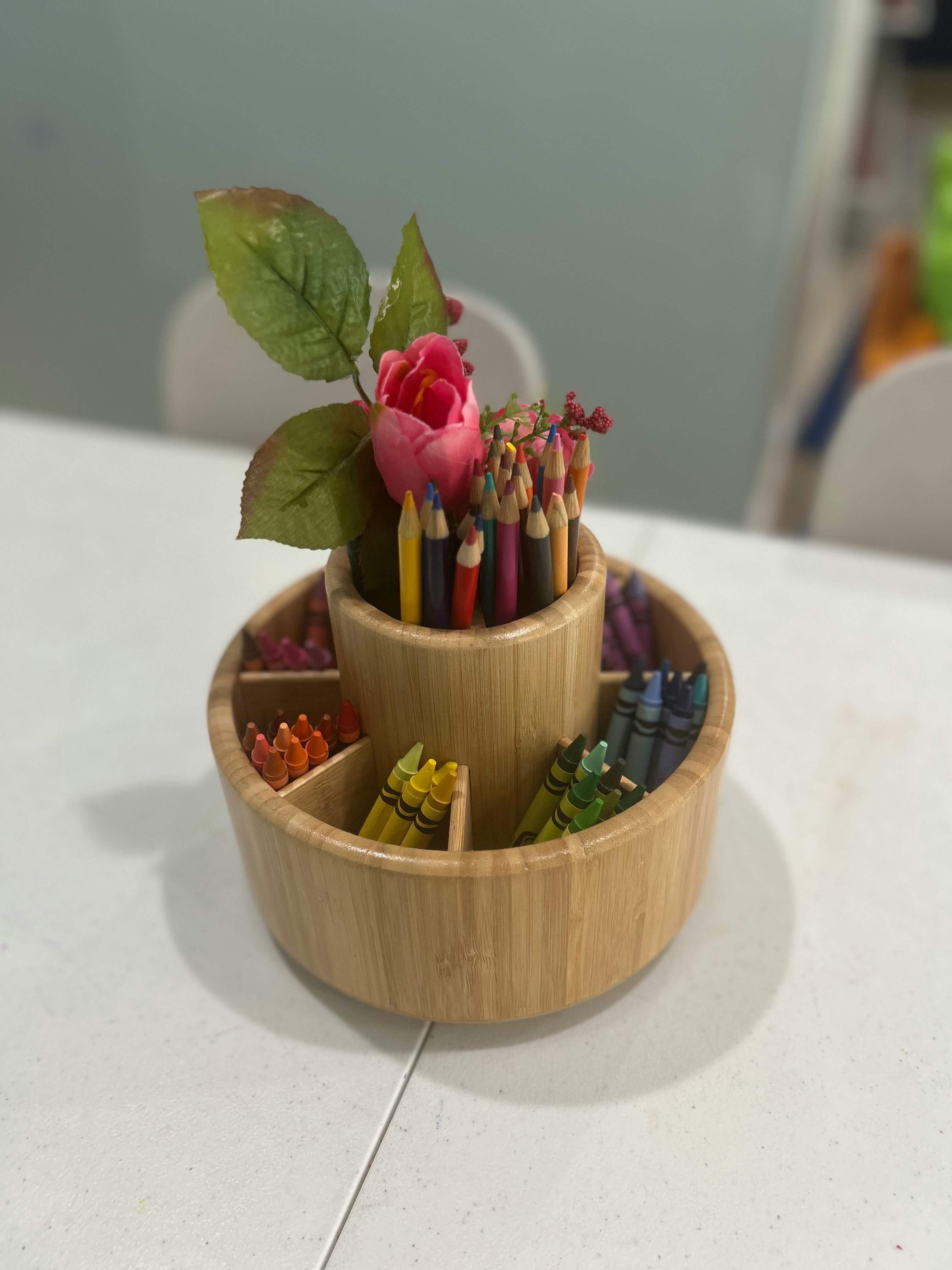 Wooden caddy with colored pencils, crayons, and a pink artificial flower