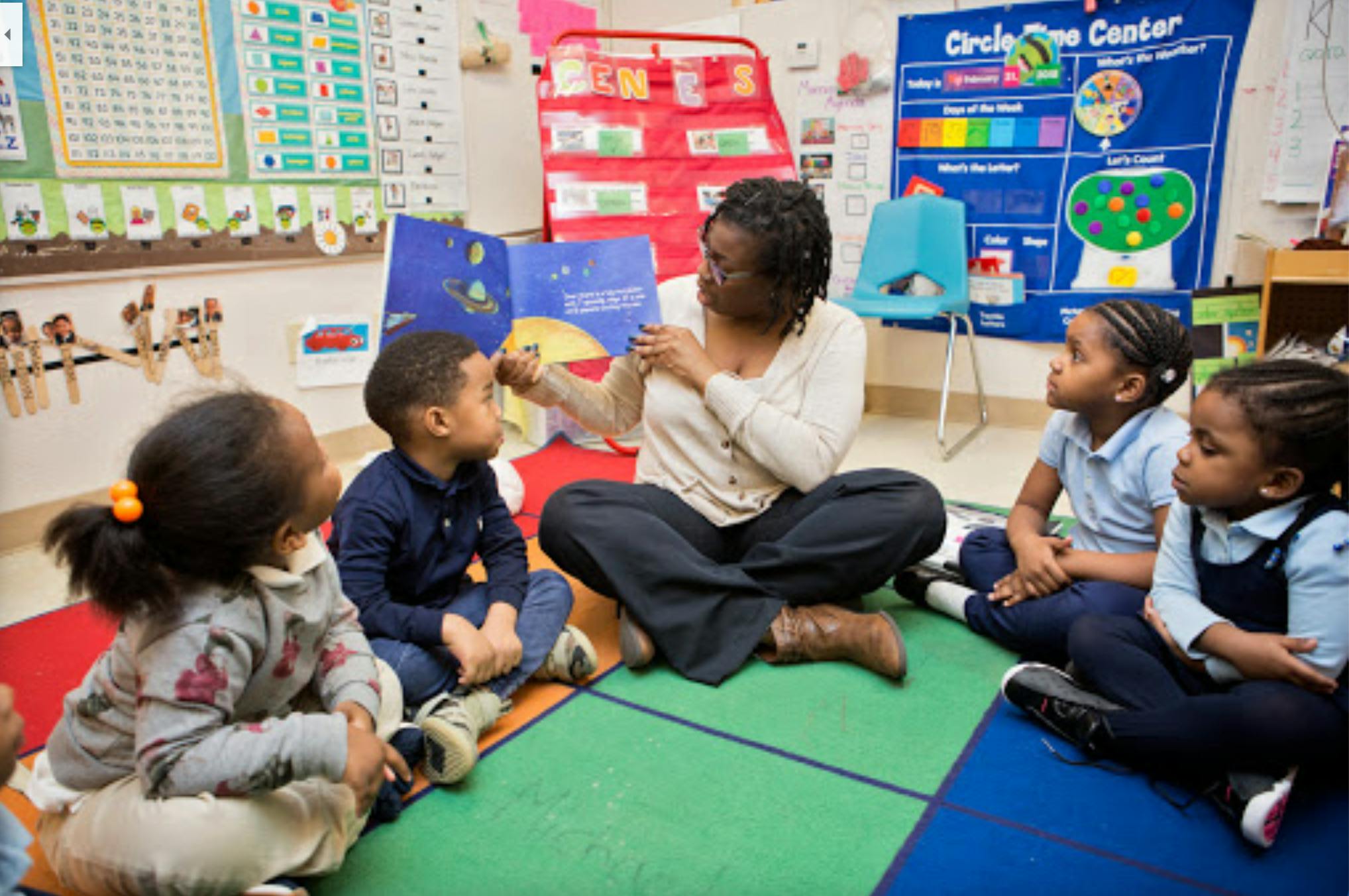 Person reading a book to four children in a classroom
