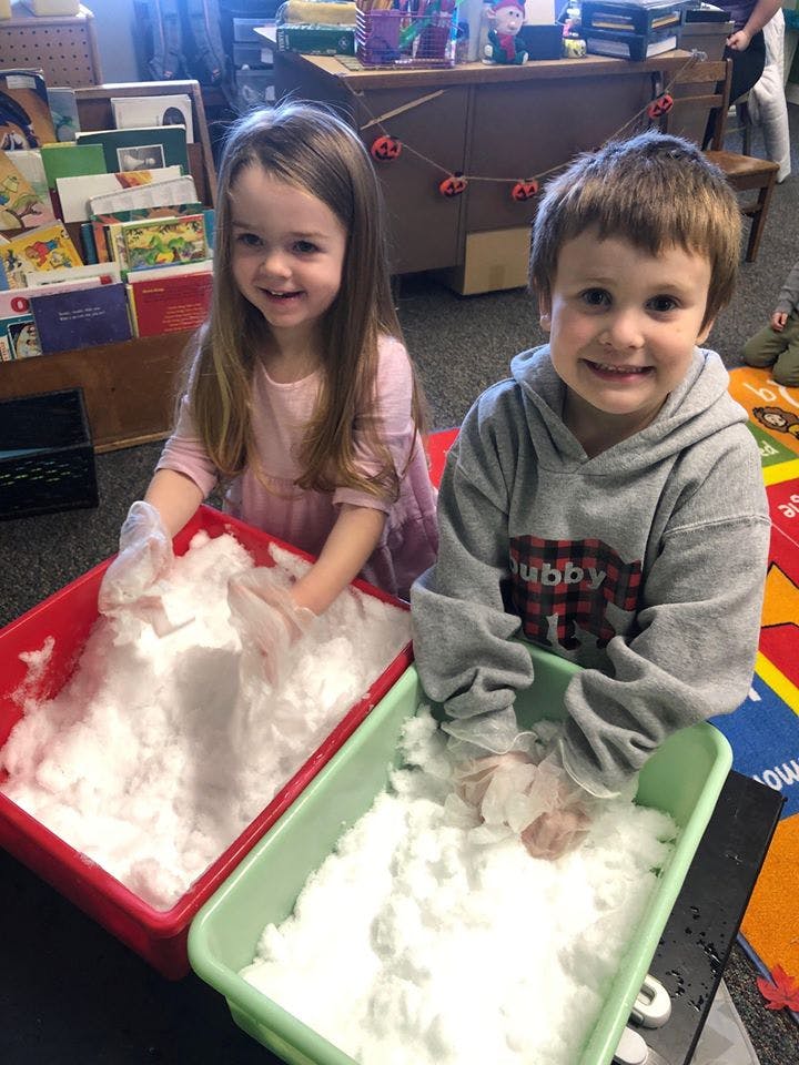 Two children playing with white fluffy material in red and green bins