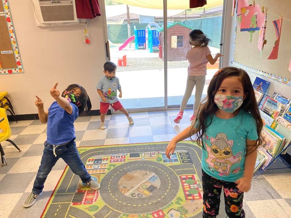 Children playing in a classroom, one child in a mask looks at the camera