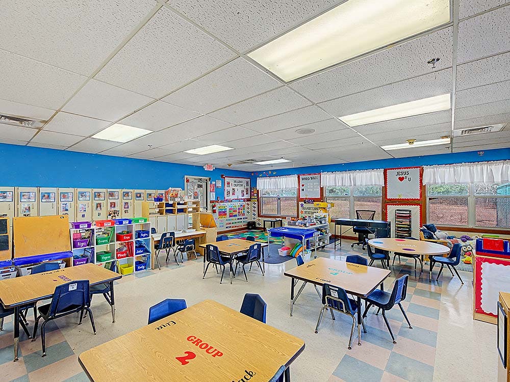 Classroom with multiple tables and chairs, artwork on walls, and large windows