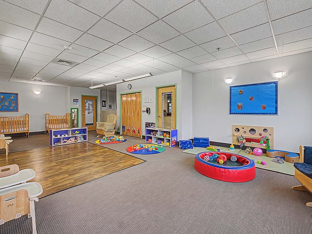 A colorful childcare room with cribs, play mats, and children's toys