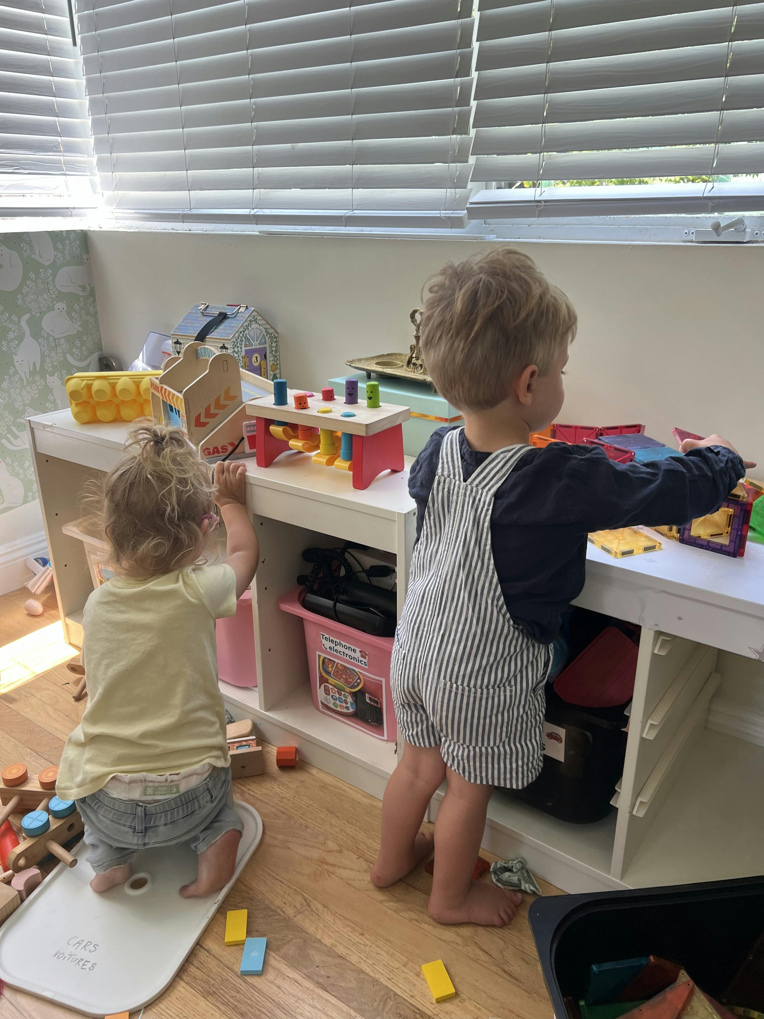 Two children playing with toys on a white shelf