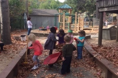 Children playing with leaves and a wheelbarrow in a playground