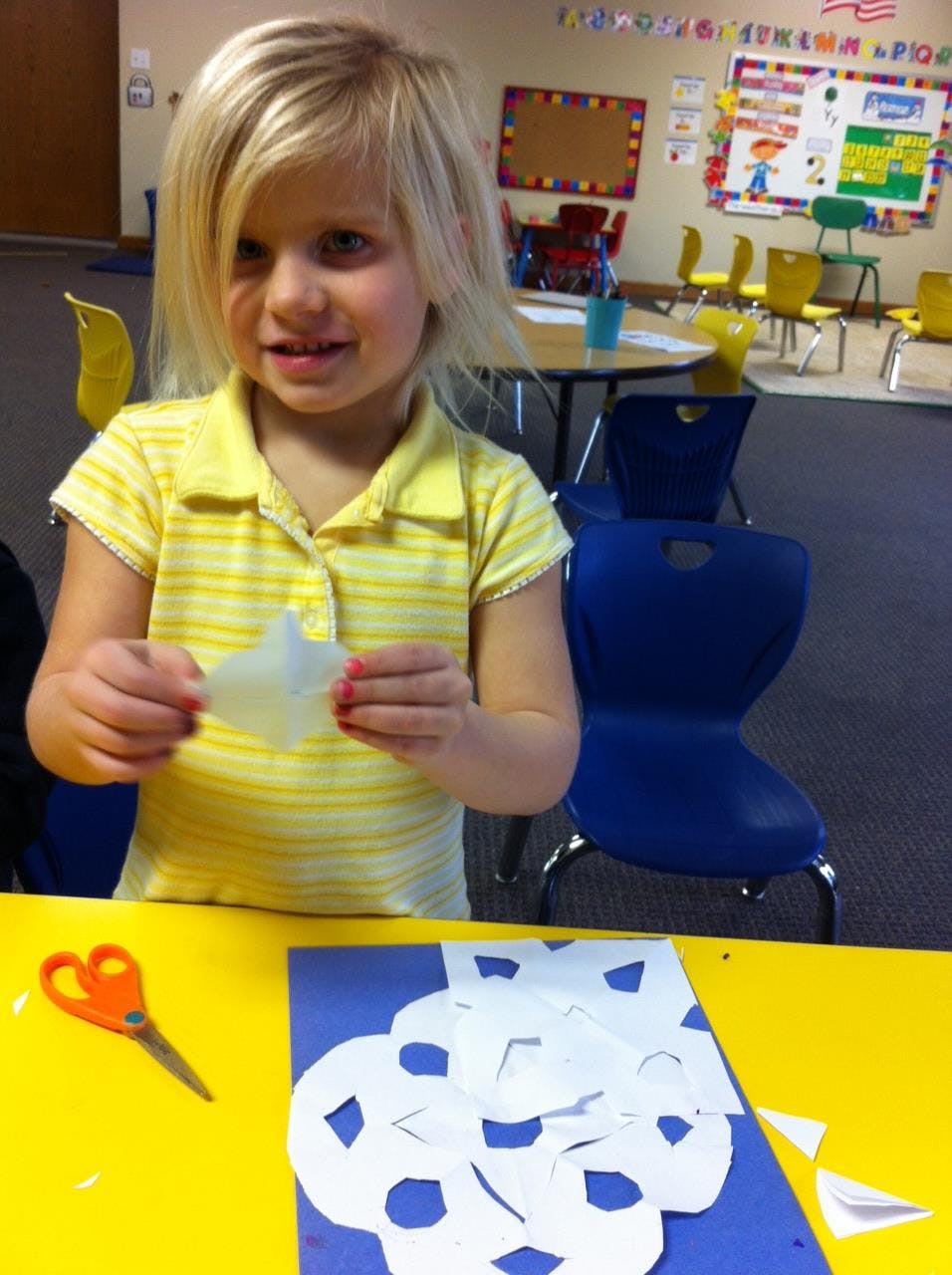 Child holding a paper cutout in a classroom