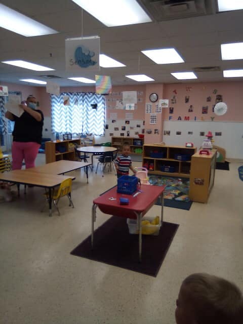 Person in mask holding paper in classroom with child