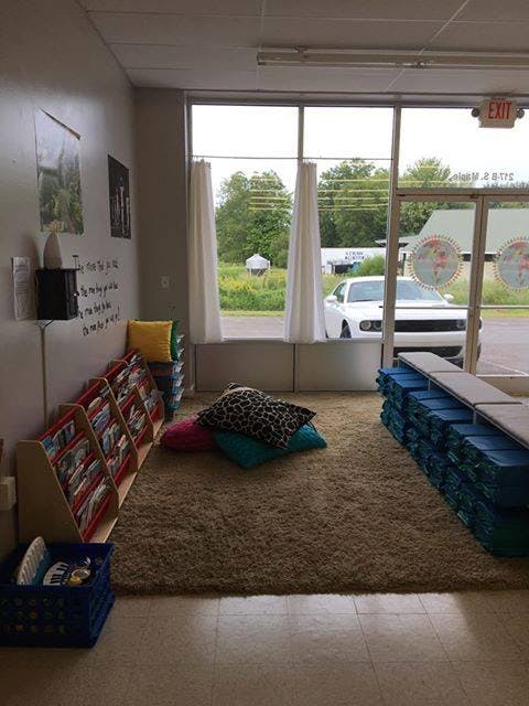 Indoor reading nook with bookshelves, pillows, and a view of a white car outside