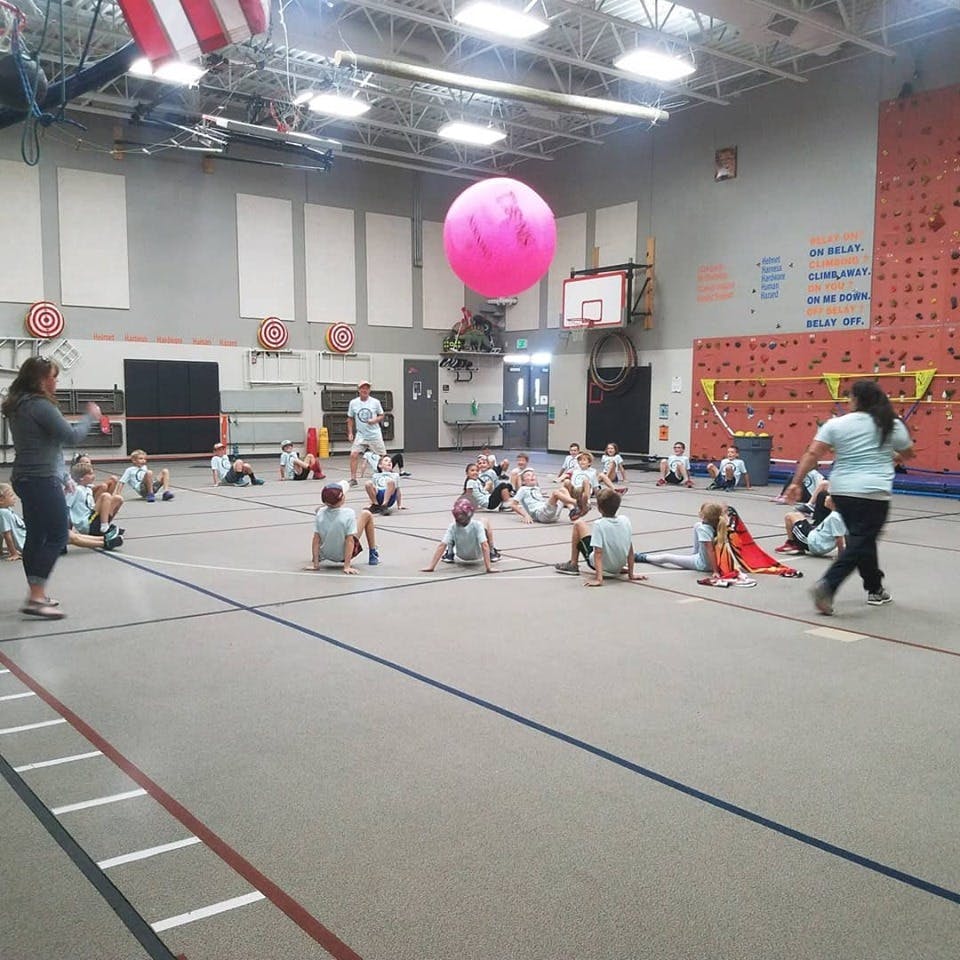 People and children sitting on a gym floor with a large pink ball overhead