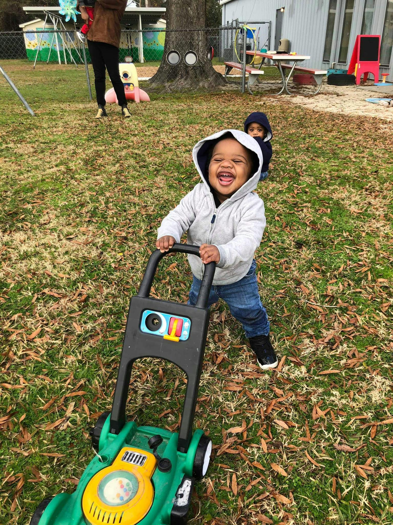 Child pushing a toy lawnmower outdoors