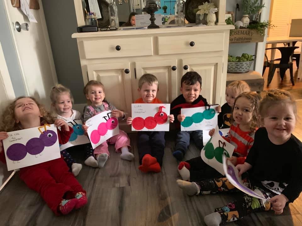 Group of children sitting on the floor holding up paper crafts