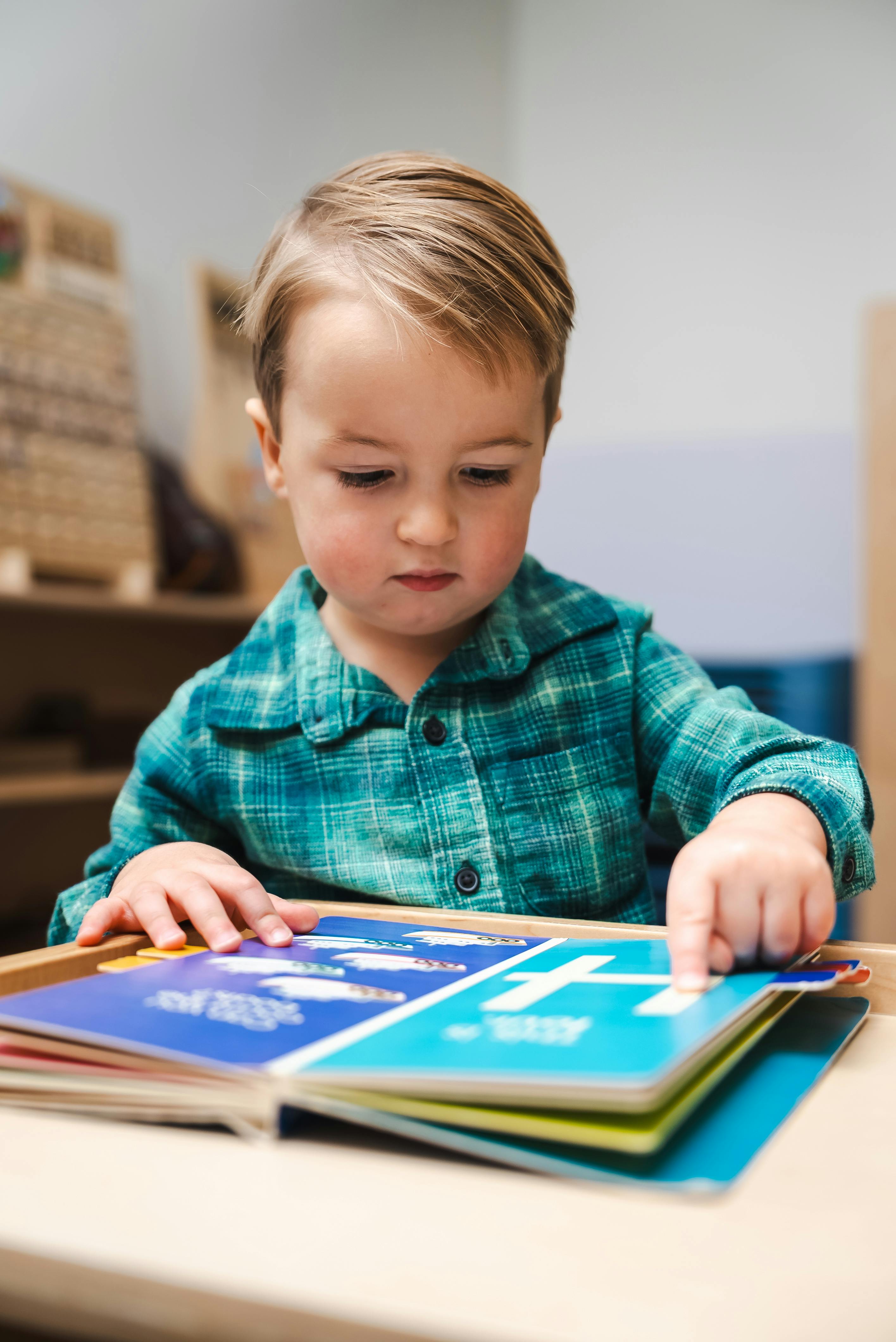 Child sitting at a table, pointing at a book