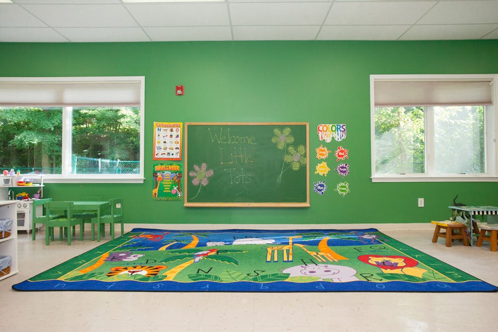 Classroom with green walls, a colorful rug, and small tables and chairs