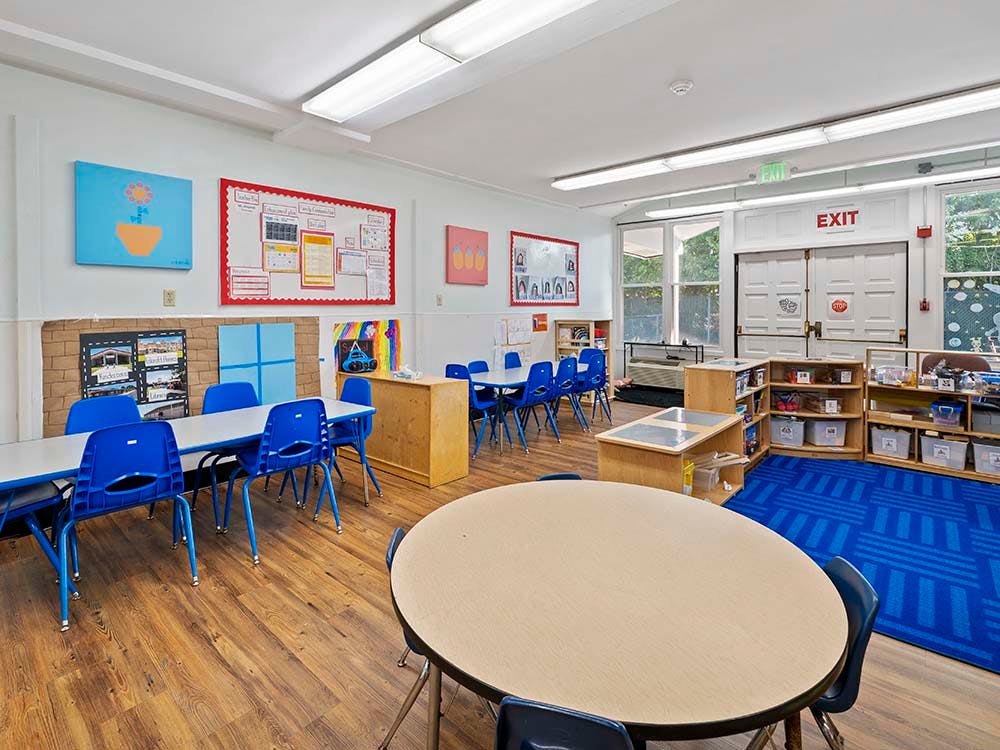 Empty classroom with tables and chairs, an exit sign above double doors