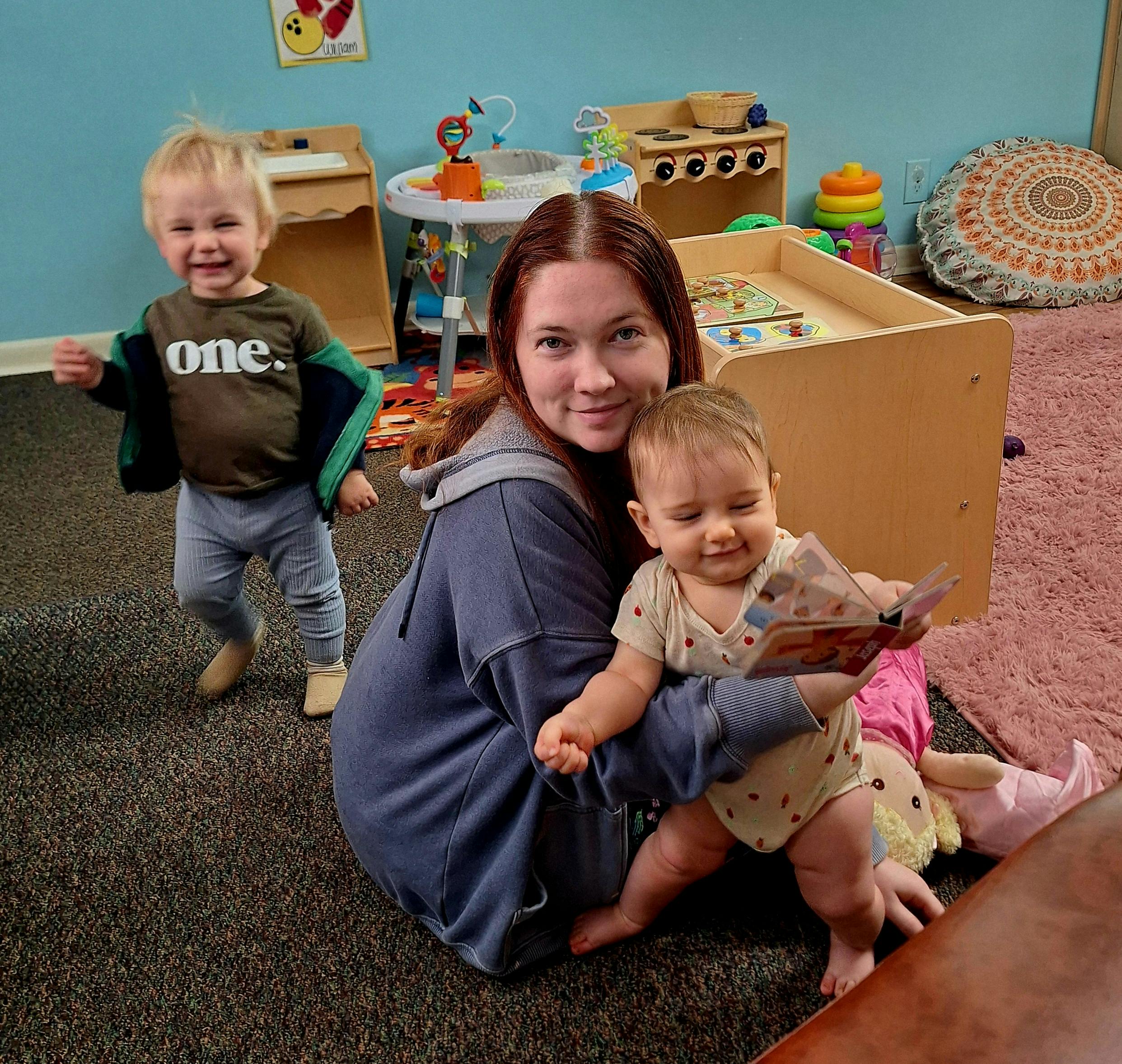 Adult holding a child with another child standing nearby in a playroom