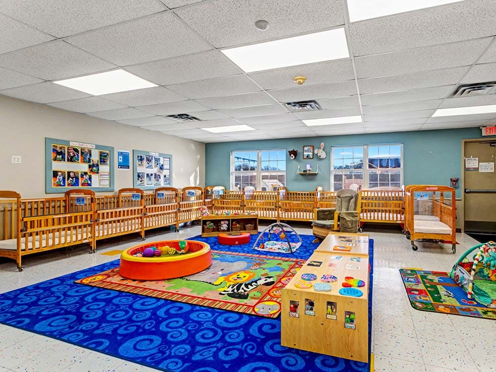 A room with multiple wooden cribs, colorful playmats, and toys
