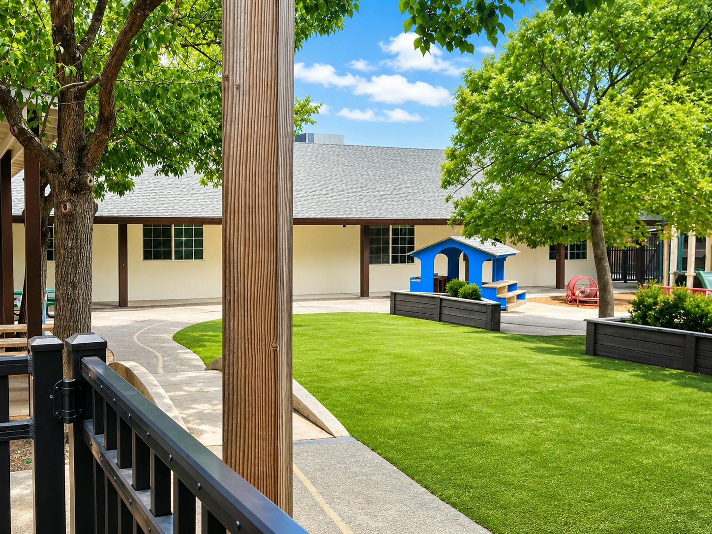 Playground area with artificial turf, a small blue playhouse, and trees